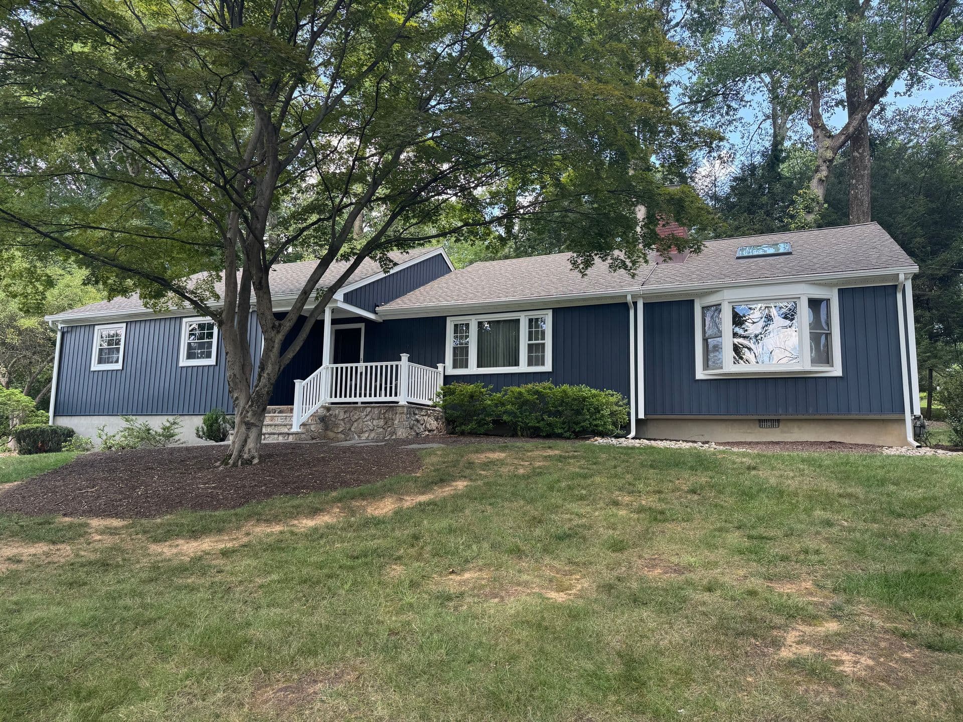 Superior Siding project — Navy board-and-batten ranch · peaked porch · mature setting
